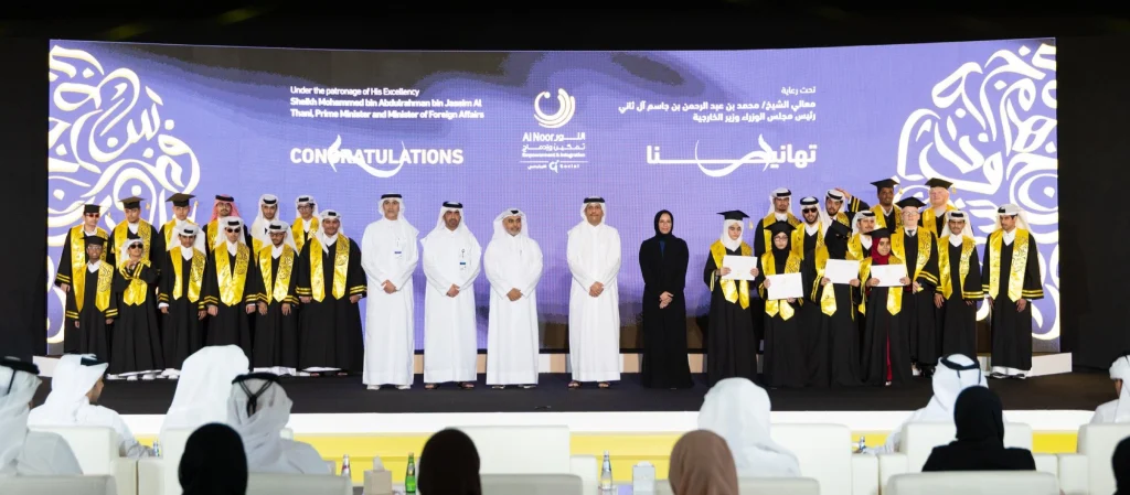 Graduates in black gowns and gold sashes celebrate on stage at the Al Noor Empowerment & Integration Programme graduation ceremony, held under the patronage of HE the Prime Minister of Qatar.