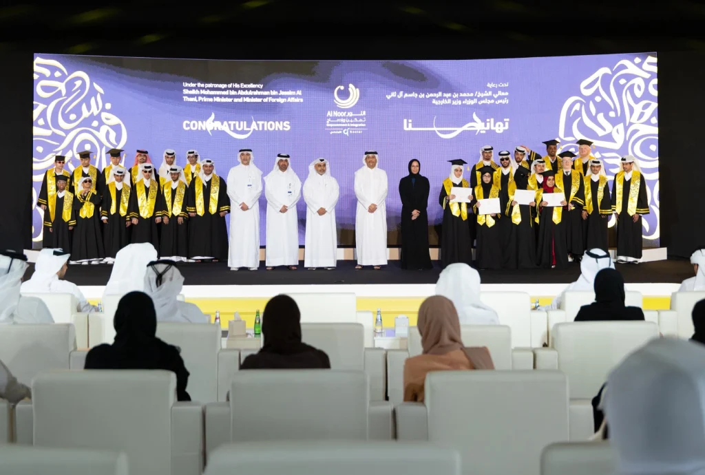 Graduates in black gowns and gold sashes celebrate on stage at the Al Noor Empowerment & Integration Programme graduation ceremony, held under the patronage of HE the Prime Minister of Qatar.