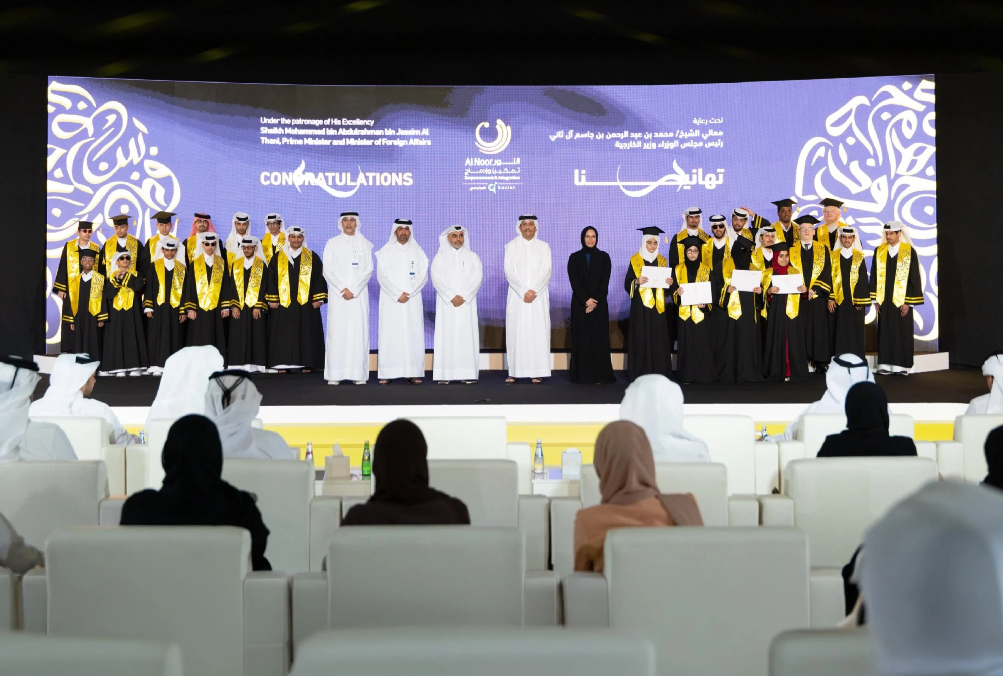 Graduates in black gowns and gold sashes celebrate on stage at the Al Noor Empowerment & Integration Programme graduation ceremony, held under the patronage of HE the Prime Minister of Qatar.